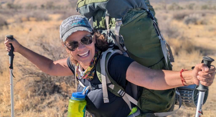 a woman wearing a backpack smiles while standing in a desert environment